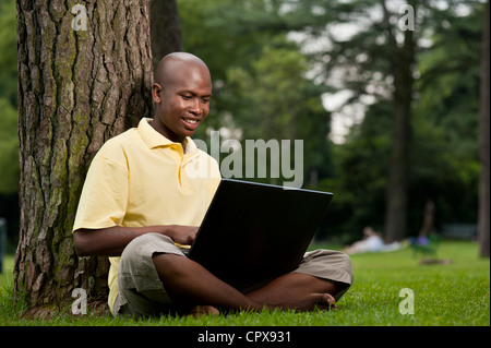 Jeune homme africain assis dans un parc, travailler sur un ordinateur portable Banque D'Images