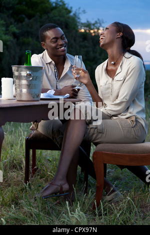 Un couple africain rire ensemble et de boire du champagne en plein air pendant le coucher du soleil Banque D'Images