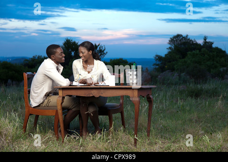 Un Africain couple chatting et boire du champagne en plein air pendant le coucher du soleil Banque D'Images