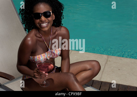 Jeune femme noire allongé sur un transat à côté d'une piscine Banque D'Images