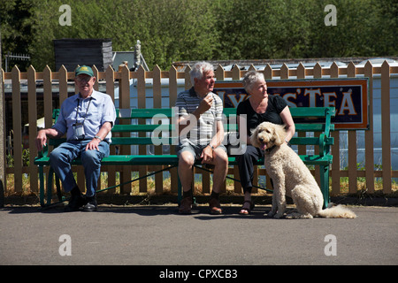 Couple assis sur un banc de travail avec chien à une extrémité et l'homme s'est assis à l'autre extrémité à la station de Corfe Castle en mai Banque D'Images