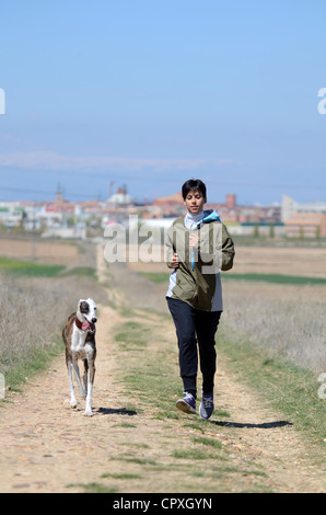 Les jeunes aux cheveux courts jogger running through field road avec son chien Banque D'Images