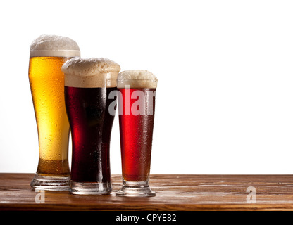 Trois verres de bières différentes sur une table en bois. Isolé sur blanc. Banque D'Images