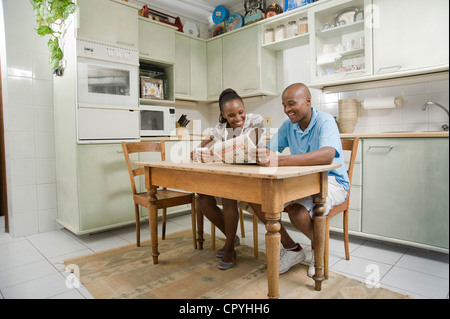Jeune couple s'asseoir ensemble dans une cuisine, lire un journal Banque D'Images