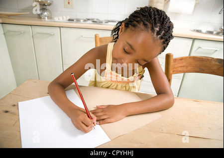 Jeune fille africaine assis dans une cuisine faire ses devoirs Banque D'Images