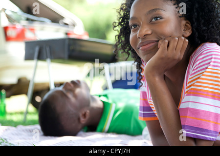 Gros plan du jeune femme noire appuyée sur sa main, avec un jeune homme noir en arrière-plan de couchage Banque D'Images