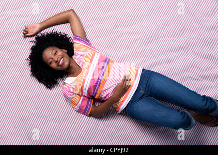 Coup de au-dessus d'une jeune femme noire couchée sur une couverture dans un parc, looking up and smiling Banque D'Images