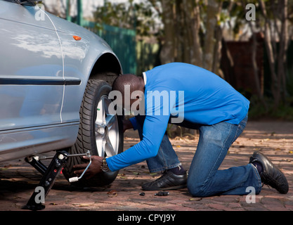 Homme africain changer le pneu sur une voiture Banque D'Images