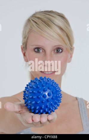 Jeune femme avec son bras tendus et tenant une balle de massage hérissés bleu dans sa main Banque D'Images