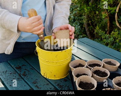 Enfant remplit des petites plantes avec du compost de planter des graines à l'aide d'un seau et une truelle. Banque D'Images