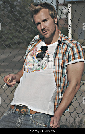 L'homme rebelle portait un jean et une chemise à carreaux à une station-service, fumeurs Banque D'Images