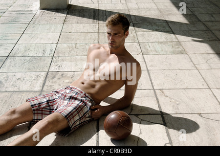 Jeune homme athlétique en shorts avec ballon allongé sur un sol en pierre Banque D'Images