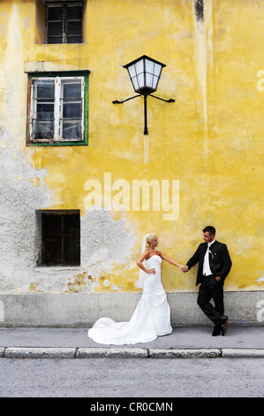 Mariage, Bride and Groom holding hands en face d'un vieux mur jaune, Banque D'Images