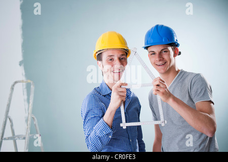 Deux jeunes commerçants tenant une règle de charpentier de pliage en forme d'une maison Banque D'Images