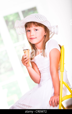 Jeune fille vêtue d'une robe blanche et un chapeau, manger une glace Banque D'Images