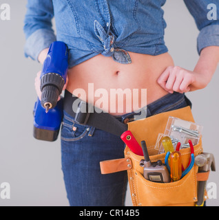 Close up of young woman wearing tool belt et holding drill, studio shot Banque D'Images