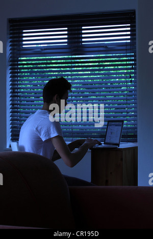 Jeune homme assis dans une pièce sombre à l'aide d'un ordinateur portable. Banque D'Images