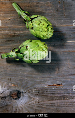 Deux Artichauts (Cynara cardunculus) sur une surface en bois rustique Banque D'Images