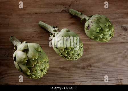 Trois artichauts (Cynara cardunculus) sur une planche en bois Banque D'Images