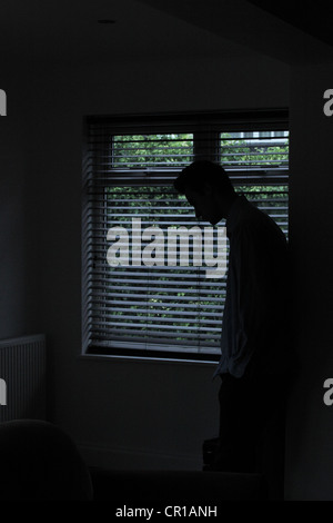 Silhouette d'un homme debout dans une pièce sombre avec la lumière d'une fenêtre avec stores montrant sa forme. Banque D'Images