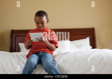 Boy playing handheld video game on bed Banque D'Images