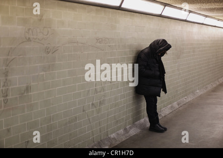 Personne à capuchon s'appuyant sur le mur du métro Banque D'Images