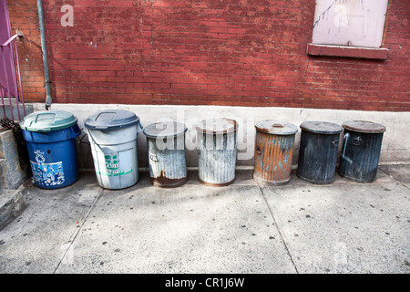 L'ancienne ligne de poubelles galvanisées avec traces de peinture alignés contre un mur de briques Hells Kitchen quartier NYC Banque D'Images