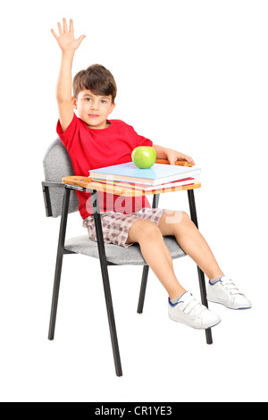 Un portrait d'un écolier assis sur une chaise levant la main isolé sur fond blanc Banque D'Images