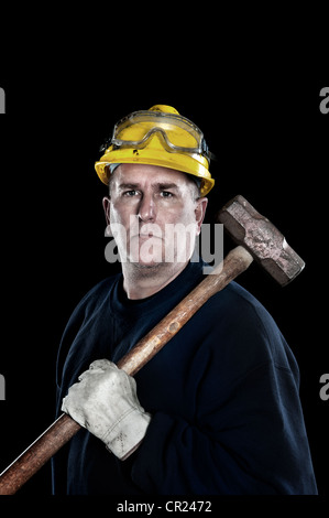 Un ouvrier manuel avec une masse jaune portant un casque de protection et des gants de travail protecteurs isolated on black Banque D'Images