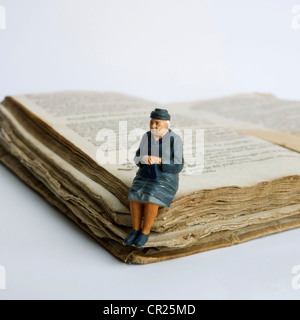 Dame âgée, miniature, figurine, assis sur un vieux livre. Banque D'Images