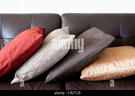 Quatre coussins colorés sur le canapé en cuir marron foncé Banque D'Images