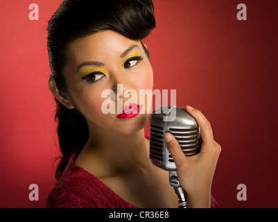 Asian woman singing into microphone Banque D'Images