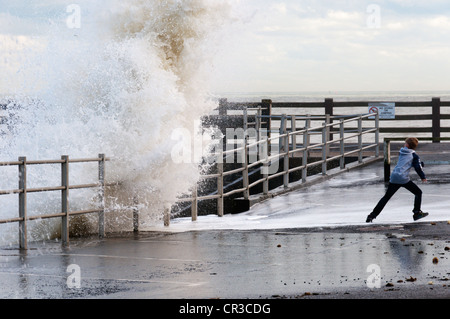 Un jeune garçon en esquivant les vagues se brisant sur le mur du port à Broadstairs dans le Kent. Banque D'Images