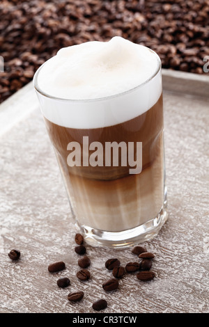 Latte macchiato dans un verre sur un plateau avec café en grains Banque D'Images