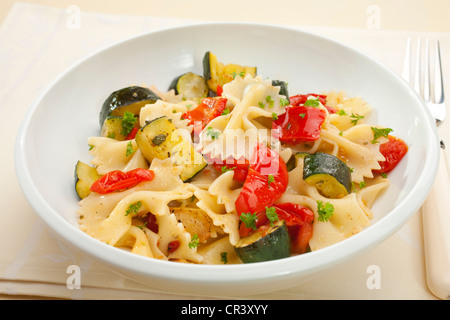 Un bol de farfalle ou farfalle avec courgettes rôti ou les courgettes, poivrons et tomates avec l'huile d'olive et des herbes. Banque D'Images