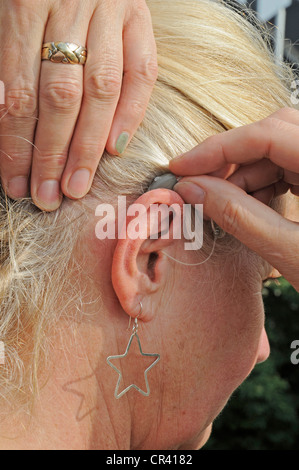 L'aide auditive moderne petit derrière l'oreille d'une femme, de 55 à 60 ans, la dureté de l'ouïe Banque D'Images