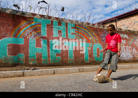 Garçon jouant au football en face de mur avec le mot "Le Ghetto", Soweto Township, Gauteng, Afrique du Sud, l'Afrique Banque D'Images