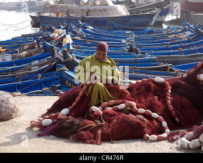 Musulman vêtu d'un caftan traditionnel raccommodage des filets de pêche dans le port d'Essaouira, Maroc, Afrique du Nord, Afrique Banque D'Images