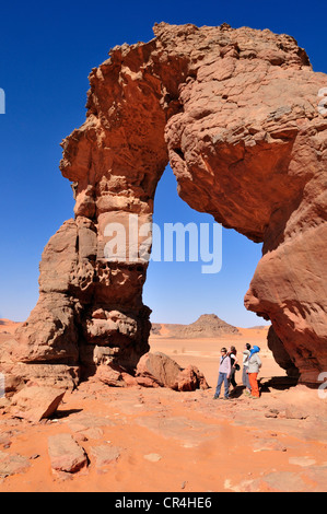 Les touristes sous le pont naturel ou arch rock d'In Tehak, montagnes ou Acacus Tadrart Acacus éventail Banque D'Images