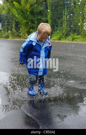 4-année-vieux garçon sautant dans une flaque d'eau sur la route sous la pluie, Assamstadt, Bade-Wurtemberg, Allemagne, Europe Banque D'Images