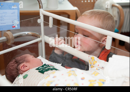 Garçon, 2 ans, regarder un bébé endormi dans la maternité dans un hôpital Banque D'Images