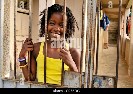 Smiling girl debout derrière une porte en treillis, Favela Morro da Formiga slum, district de Tijuca, Rio de Janeiro, Brésil Banque D'Images