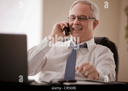 Caucasian businessman talking on cell phone at desk Banque D'Images