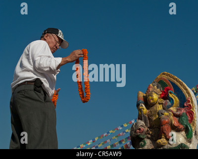 L'homme local offrant une guirlande de fleurs à l'image d'une déesse, Boudnath, Katmandou, Népal, Asie du Sud Banque D'Images