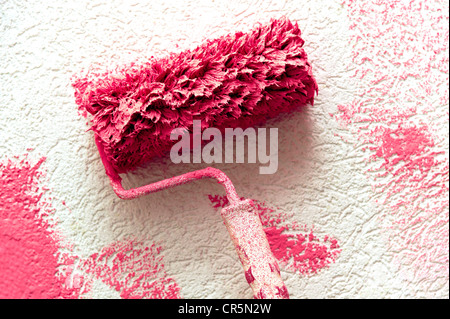 Rouleau à peindre avec peinture rose sur un mur blanc Banque D'Images