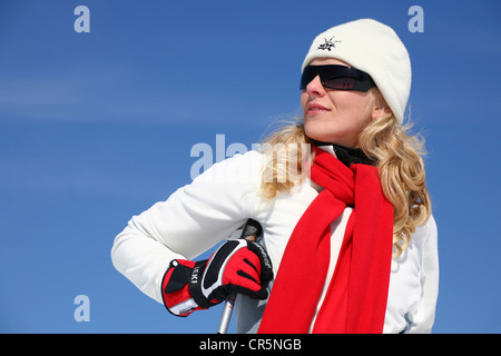 Jeune femme, environ 25 ans, portant un manteau, un chapeau, des lunettes et une écharpe rouge, against a blue sky Banque D'Images
