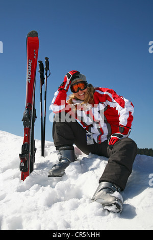 Jeune femme, environ 25 ans, assis dans la neige, skis et bâtons de ski bloqué dans la neige, forêt de montagne Banque D'Images