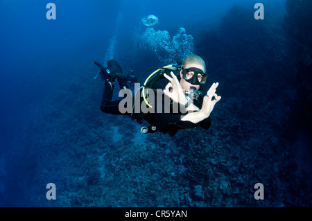 Plongeur mâle nage en eau bleu clair et rend le signe OK Banque D'Images