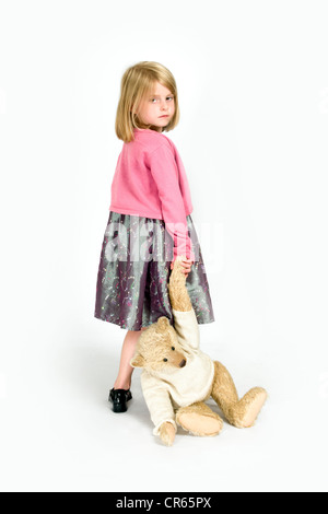 Studio image d'un malheureux Caucasian 7 ans, fille, faisant glisser un ours sur un fond blanc, concept de mec Banque D'Images