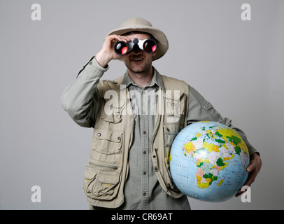 Jeune homme regardant à travers des jumelles et holding globe against white background Banque D'Images